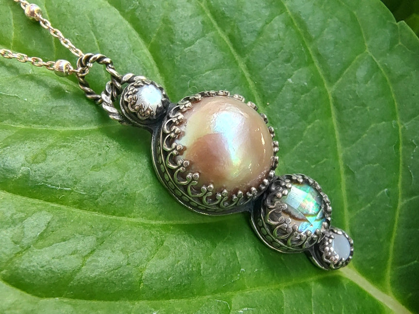 A pendant with pink pearl, abalone and shell on a green leaf