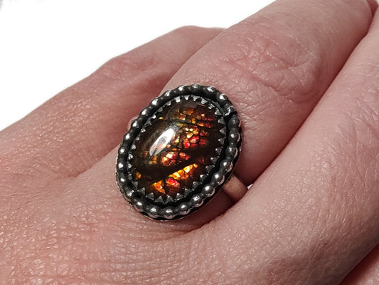 Close-up of a hand wearing a decorative ring with an ammolite gemstone.