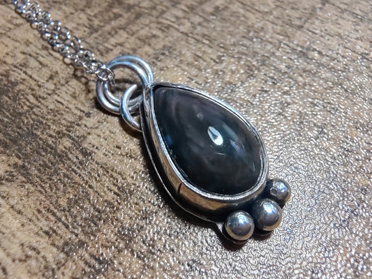 Silver necklace with a velvet obsidian teardrop pendant on a wooden surface