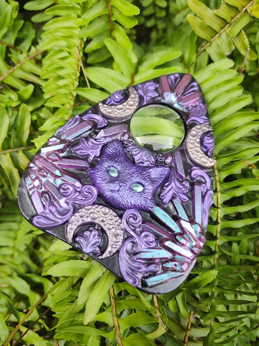 Decorative planchette with pink to blue crystal pattern and cat with crescent moons on a green leaf