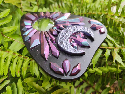 Decorative planchette with pink to blue chameleon crystal pattern and crescent moon on a green leaf background