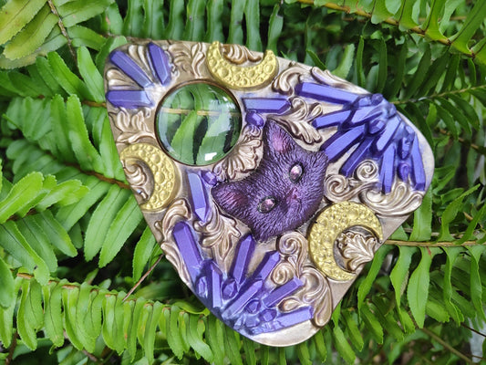 Decorative planchette with purple and gold cat design on green leaves