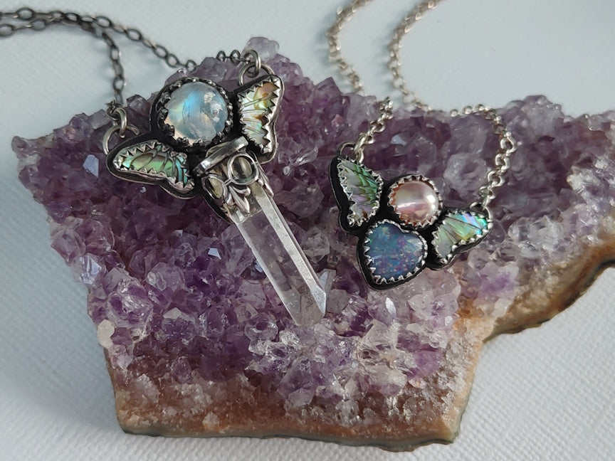 Two butterfly-themed necklaces on a piece of amethyst crystal.