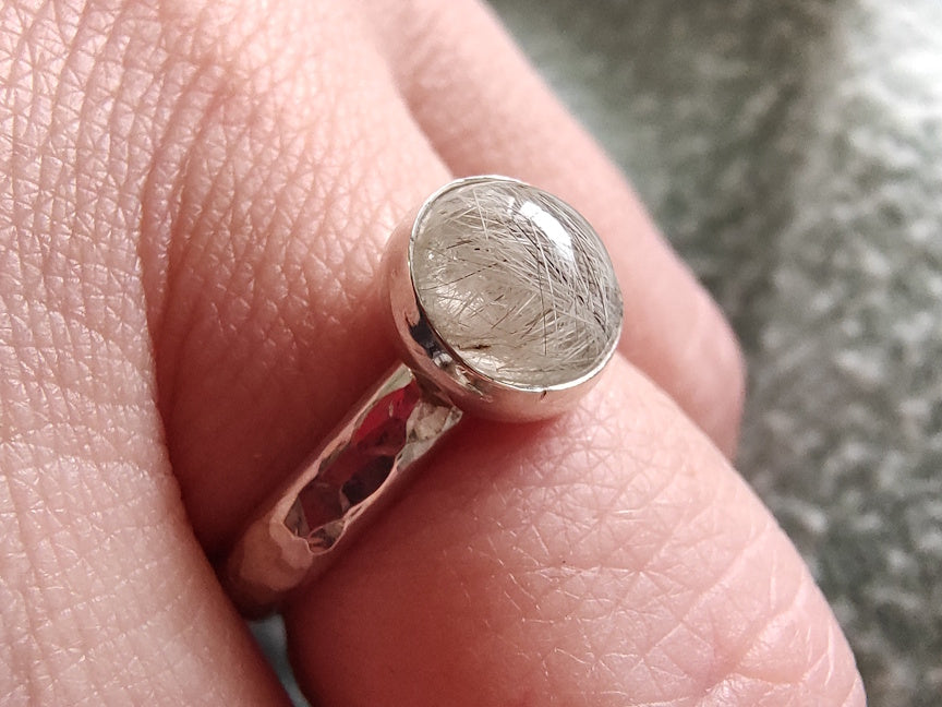Sterling silver memorial ring with pet fur, worn on a pale finger.
