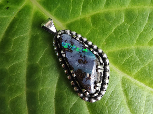 Yowah boulder opal pendant necklace on a chain with a green leafy background.