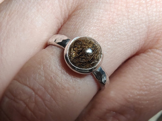 Closeup shot of a memorial ring with hammered sterling band, being worn on a pale hand.