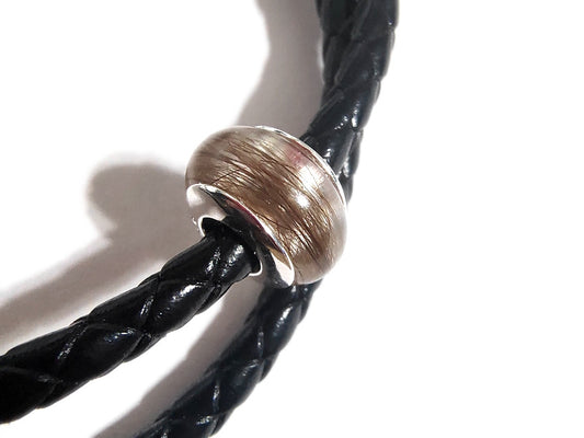 closeup of a memorial bead with light colored hair on a black braided leather bracelet