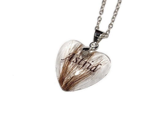 A small heart shaped pendant with the name Astrid and a small amount of hair inside.