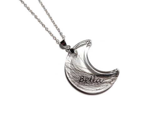 Clear crescent moon necklace with 'Bella' name and small amount of fur on a white background, strung on sterling chain.