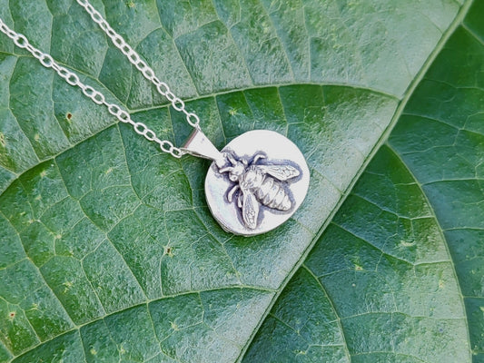 Reverse view of a handmade sterling pendant with bee detail, atop a large green leaf.