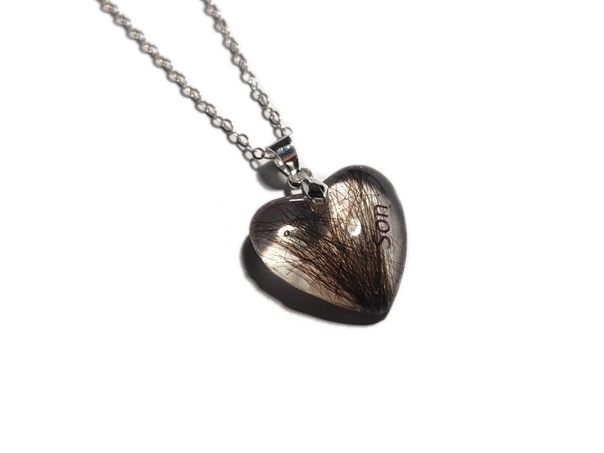 A small heart shaped pendant with tuft of hair and the name Son.