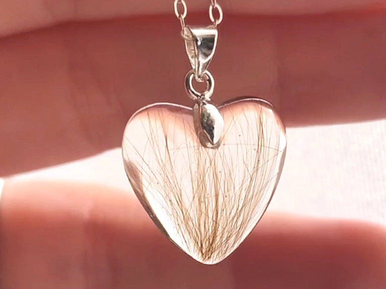 A memorial hair keepsake pendant in heart shape, held between fingers.