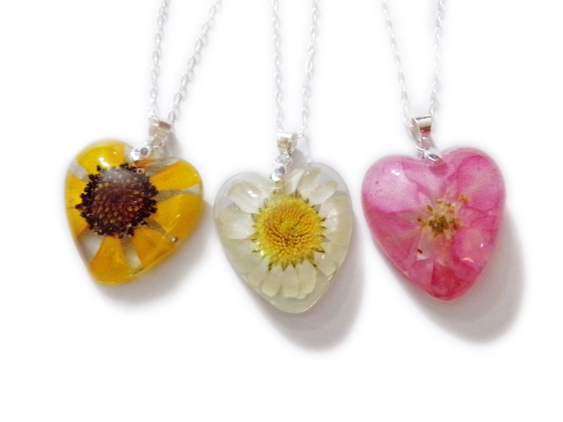 Nature inspired necklaces. Trio of resin heart shaped necklaces. From left to right- yellow daisy with brown center, white daisy with yellow center, pink larkspur. 