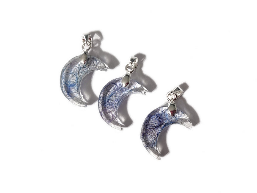 A trio of tiny moon hair memorial pendants with blue hair.