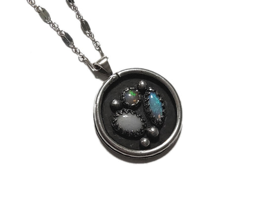 Silver necklace with a round pendant featuring embedded stones on a white background