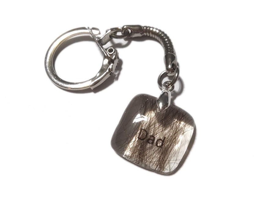 A small square memorial keychain containing hair and the name Dad.
