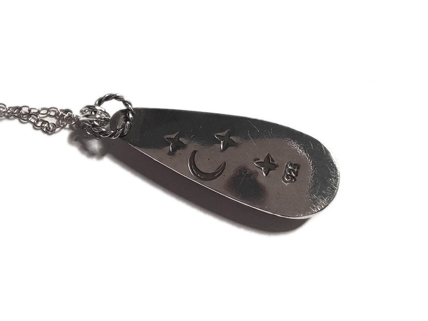 Silver pendant with stamped moon and star symbols on a white background