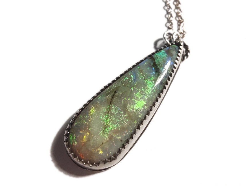 Teardrop-shaped opal pendant on a chain against a white background