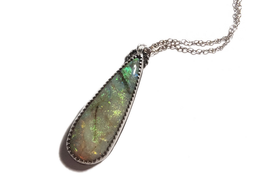 Teardrop-shaped opal pendant on a silver chain against a white background