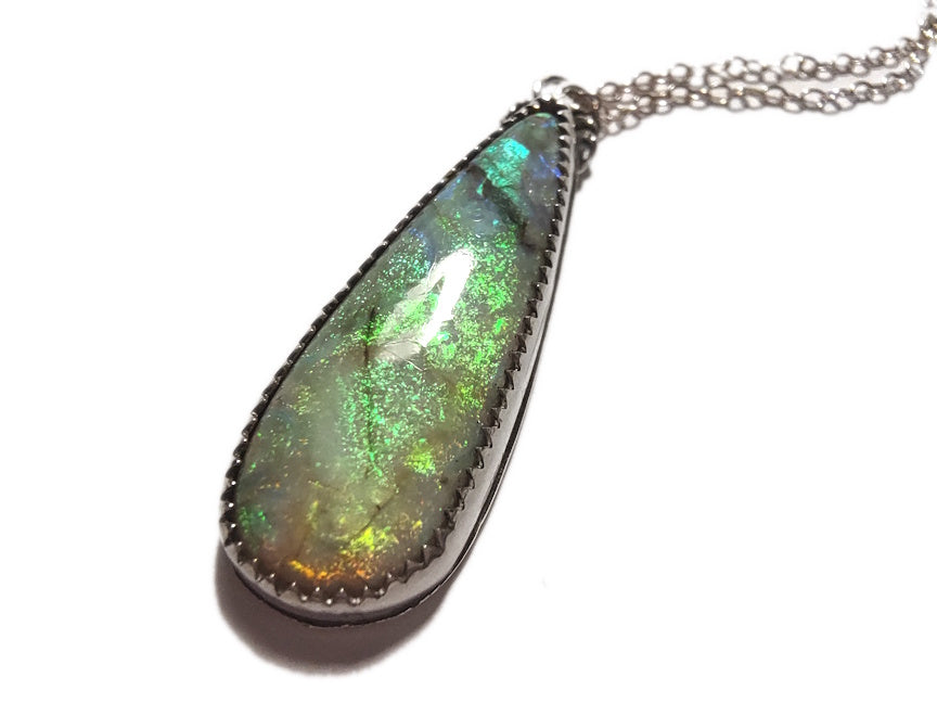 Teardrop shaped opal pendant in silver with a white background