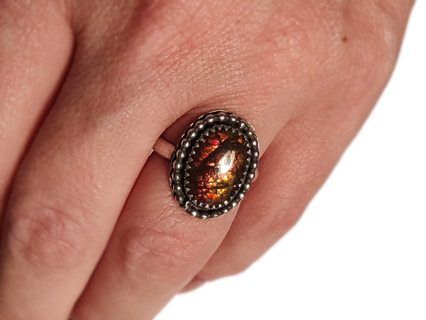Close-up of a hand wearing a decorative ring with an ammolite gem