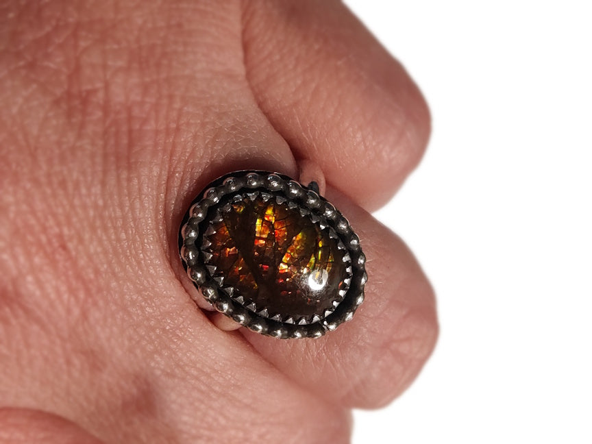 Close-up of a ring with an ammolite on a person's finger against a white background