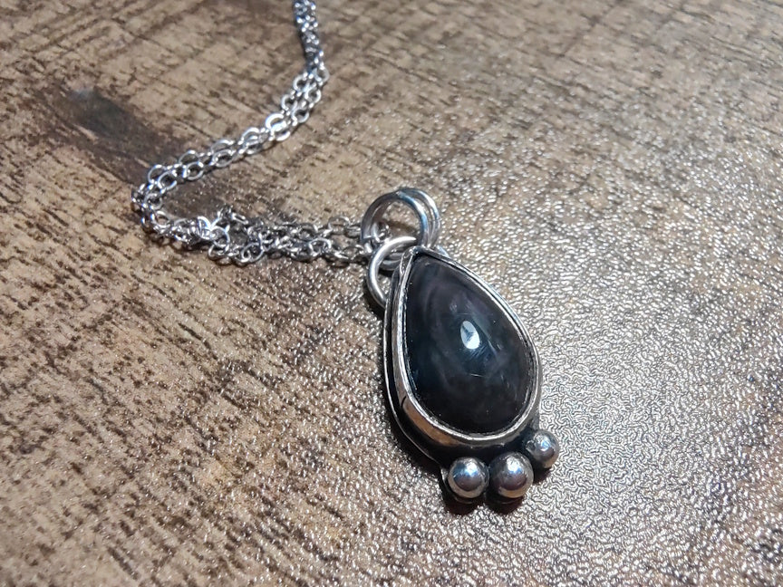 Necklace with a black teardrop pendant on a textured wooden surface