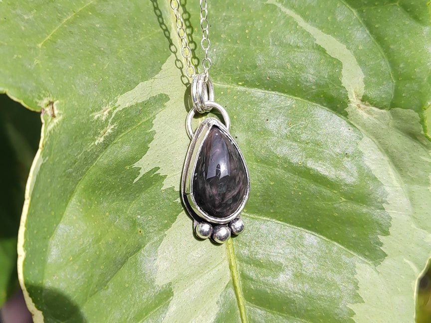 Teardrop-shaped pendant on a chain with silver setting, placed on a green leaf.
