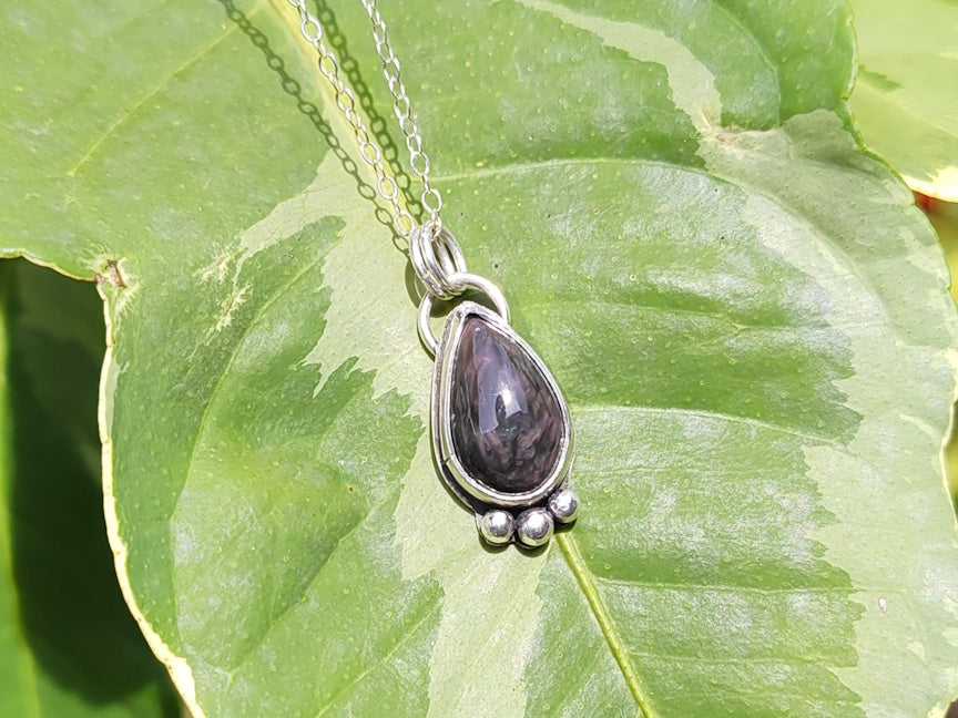 Silver pendant with a purple stone on a green leaf