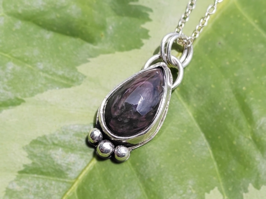 Silver pendant with a velvet obsidian stone on a green leaf background