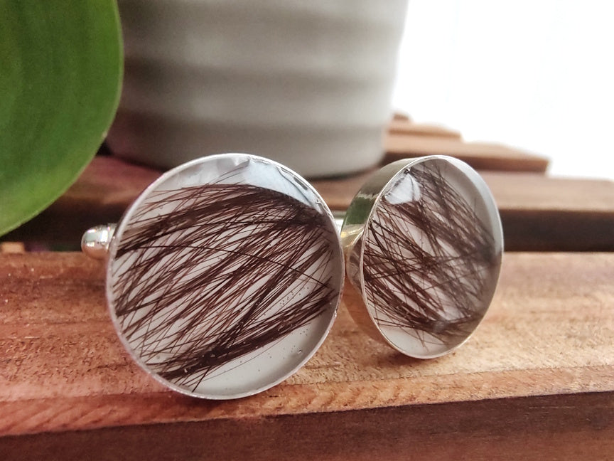 Cufflinks with hair strands on a wooden surface