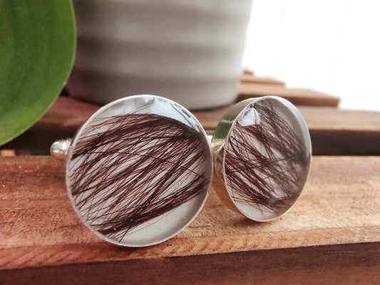 Cufflinks with hair strands on a wooden surface