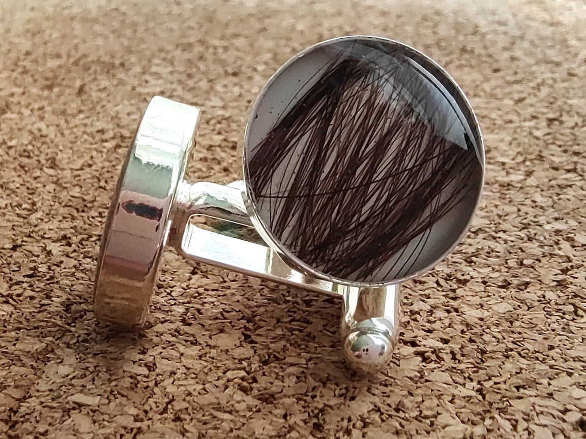 Silver cufflinks with hair in a round setting on a cork background
