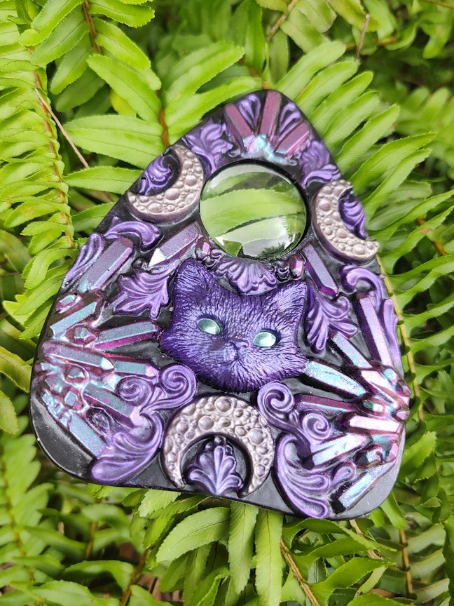 Decorative planchette with pink to blue crystal pattern and cat with crescent moons  on a green leaf 
