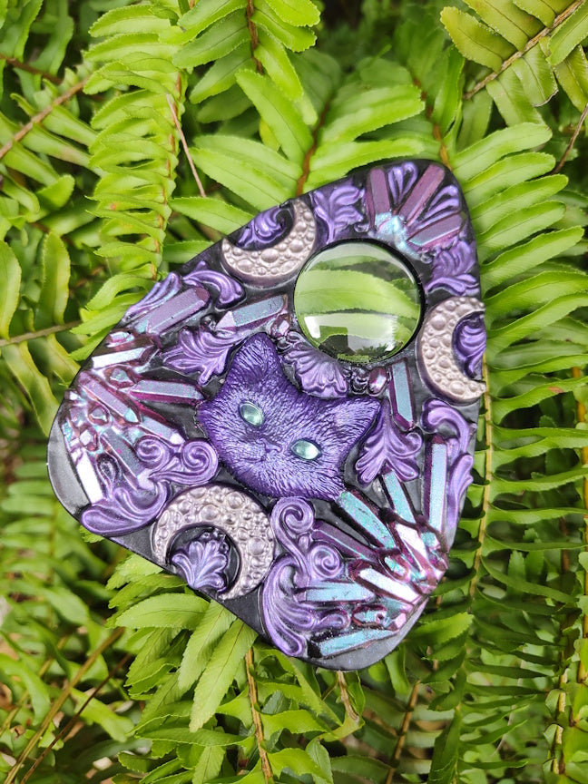 Decorative planchette with pink to blue crystal pattern and cat with crescent moons  on a green leaf 