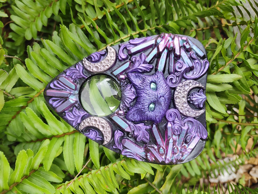 Decorative planchette with pink to blue crystal pattern and cat with crescent moons  on a green leaf 