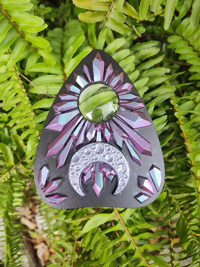 Decorative planchette with pink to blue chameleon crystal pattern and crescent moon on a green leaf 