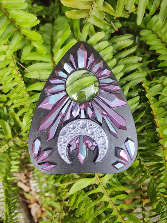 Decorative planchette with pink to blue chameleon crystal pattern and crescent moon on a green leaf 