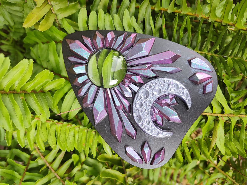 Decorative planchette with pink to blue chameleon crystal pattern and crescent moon on a green leaf 
