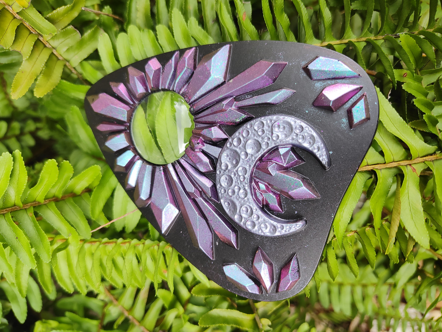 Decorative planchette with pink to blue chameleon crystal pattern and crescent moon on a green leaf 