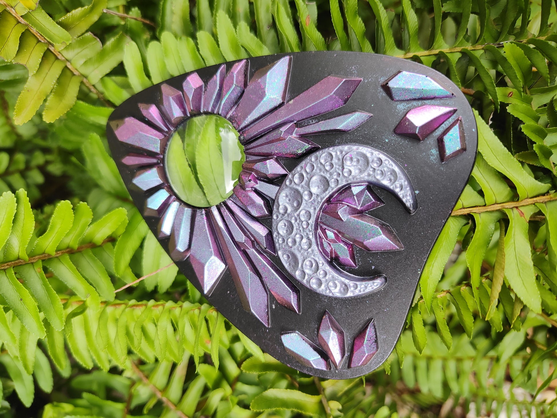 Decorative planchette with pink to blue chameleon crystal pattern and crescent moon on a green leaf 