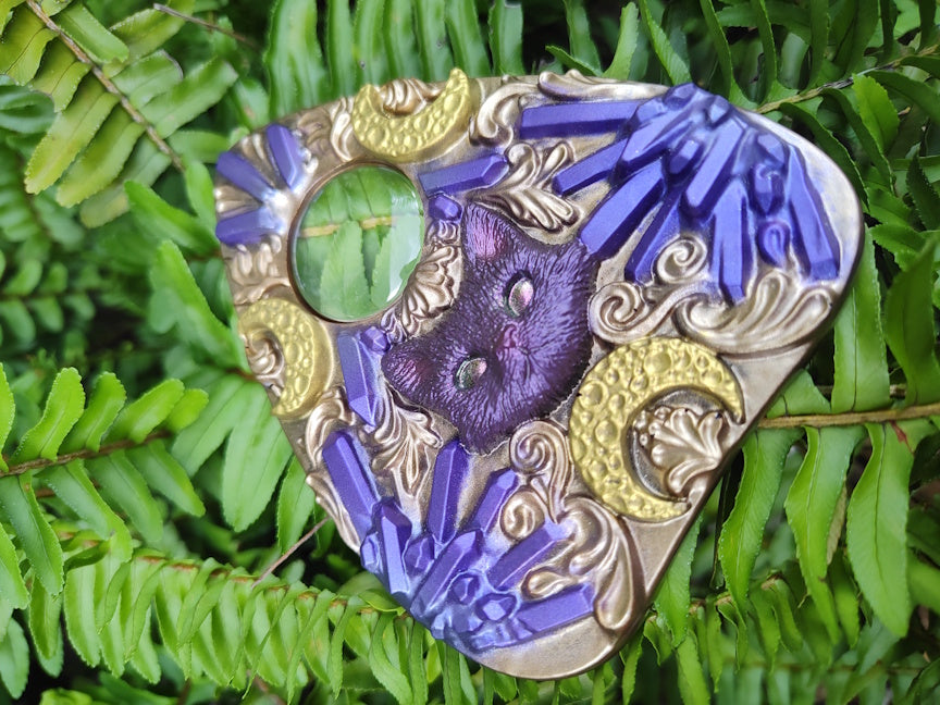 Decorative planchette  with purple and gold designs on a green leaf background