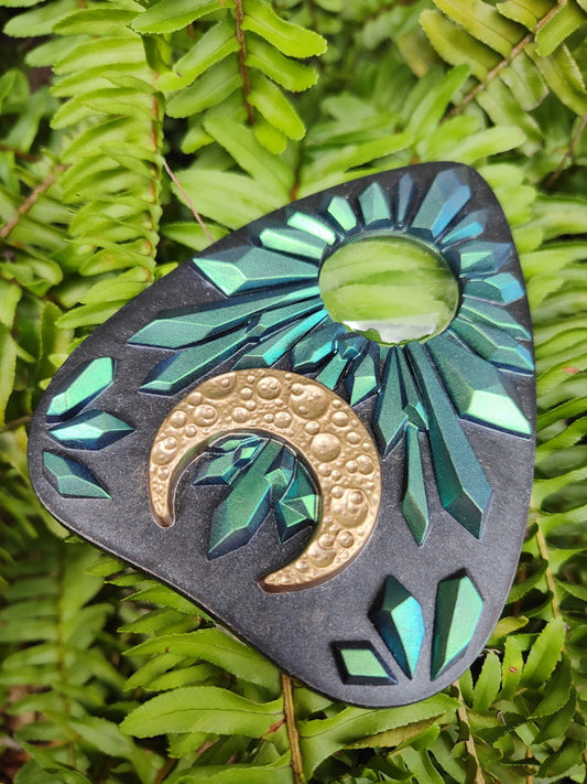 Decorative planchette with green and gold design on a green leaf background