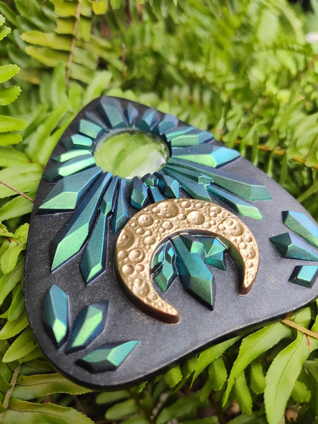 Decorative planchette with blue to green crystal design and gold crescent moon on green leaves