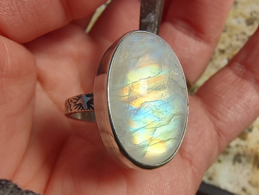 Large rainbow moonstone ring being displayed in jeweler's grip at workbench.