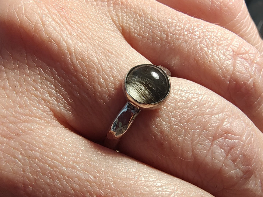 Close-up of a hand wearing a ring with a dark hair on a light skin background