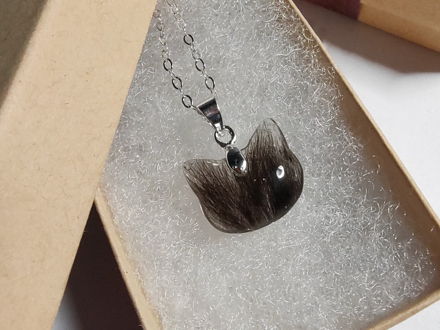 A cat shaped keepsake necklace containing dark fur in a giftbox.