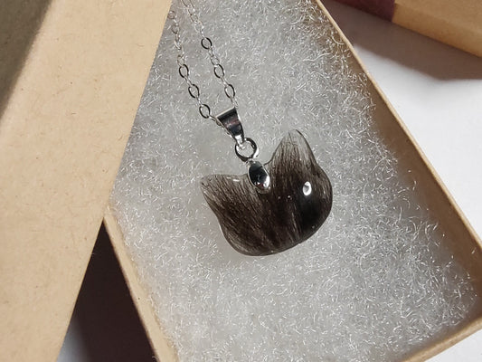 A cat shaped keepsake necklace containing dark fur in a giftbox.