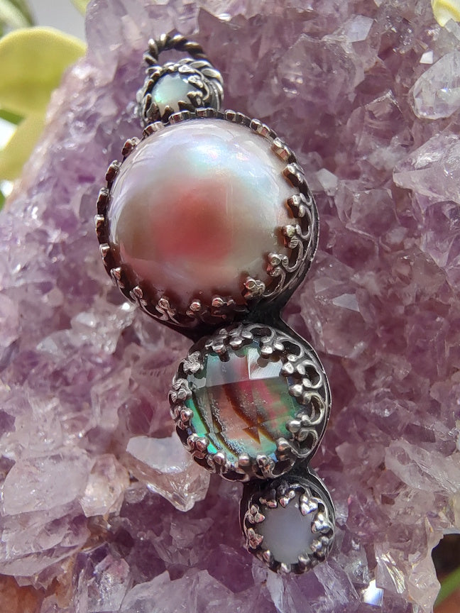 Close up view of a sterling pendant with pink pearl and abalone, sitting on an amethyst crystal.