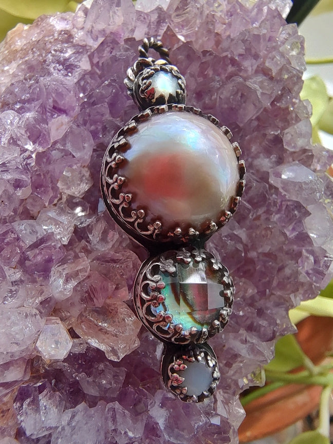 Close up view of a sterling pendant with pink pearl and abalone, sitting on an amethyst crystal.